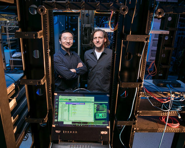 This is a photo of professors Kai Zeng and Jim Jones in their cyber security research lab. There are wires and a computer. 